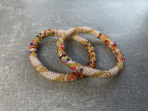 Unikke håndlavet nepal armbånd af glasperler- Som er knyttet perle for perle – Af Nepalesiske Kvinder.  Kvindegrupper i Nepal, Kathmandu Valley, udstyres med glasperler og bomuldsgarn, så de i deres fritid kan håndknytte de smukke perlearmbånd. Hvert armbånd er et unikt resultat af kvindernes håndarbejde og varierer i farvekombinationer og mønstre. De er hæklet med en bomuldssnor. Syntes man at de lidt stramme, kan man vride forsigtigt i dem så de bliver større. syntes man derimod at de er blive lidt for løse, kan man ligge dem i vand. dette gør at bomuldssnoren trækker sig sammen og de bliver mindre igen. Unikke håndlavet nepal armbånd, som er knyttet perle for perle, af nepalesiske kvinder. Vi har mere end 200 forskellige, at vælge i mellem. Så du kan finde de helt rigtige roll on nepal perle armbånd.