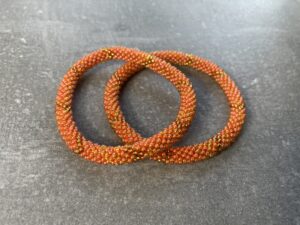 Unikke håndlavet nepal armbånd af glasperler- Som er knyttet perle for perle – Af Nepalesiske Kvinder.  Kvindegrupper i Nepal, Kathmandu Valley, udstyres med glasperler og bomuldsgarn, så de i deres fritid kan håndknytte de smukke perlearmbånd. Hvert armbånd er et unikt resultat af kvindernes håndarbejde og varierer i farvekombinationer og mønstre. De er hæklet med en bomuldssnor. Syntes man at de lidt stramme, kan man vride forsigtigt i dem så de bliver større. syntes man derimod at de er blive lidt for løse, kan man ligge dem i vand. dette gør at bomuldssnoren trækker sig sammen og de bliver mindre igen. Unikke håndlavet nepal armbånd, som er knyttet perle for perle, af nepalesiske kvinder. Vi har mere end 200 forskellige, at vælge i mellem. Så du kan finde de helt rigtige roll on nepal perle armbånd.