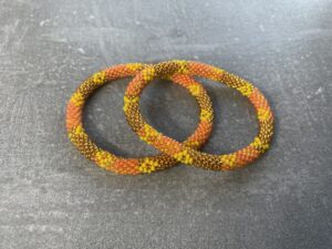 Unikke håndlavet nepal armbånd af glasperler- Som er knyttet perle for perle – Af Nepalesiske Kvinder.  Kvindegrupper i Nepal, Kathmandu Valley, udstyres med glasperler og bomuldsgarn, så de i deres fritid kan håndknytte de smukke perlearmbånd. Hvert armbånd er et unikt resultat af kvindernes håndarbejde og varierer i farvekombinationer og mønstre. De er hæklet med en bomuldssnor. Syntes man at de lidt stramme, kan man vride forsigtigt i dem så de bliver større. syntes man derimod at de er blive lidt for løse, kan man ligge dem i vand. dette gør at bomuldssnoren trækker sig sammen og de bliver mindre igen. Unikke håndlavet nepal armbånd, som er knyttet perle for perle, af nepalesiske kvinder. Vi har mere end 200 forskellige, at vælge i mellem. Så du kan finde de helt rigtige roll on nepal perle armbånd.